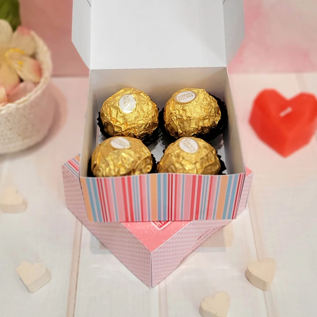 Caixa aberta colorida contendo quatro bombons dourados envolvidos em papel alumínio.