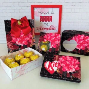 Caixas decoradas com tema romântico, laço vermelho e bombons dourados sobre superfície branca.