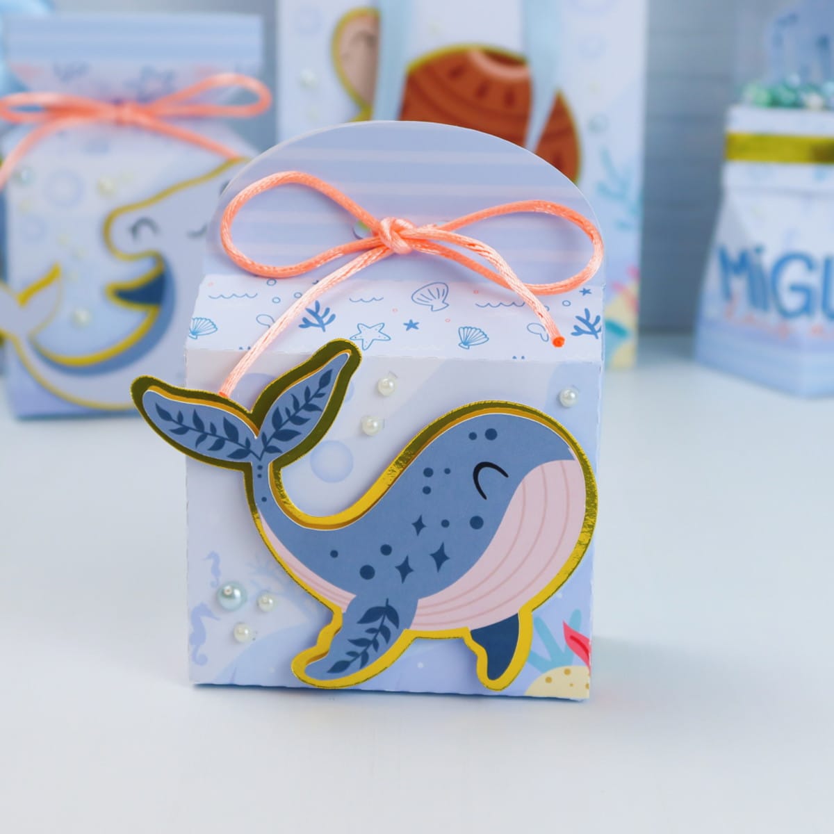 Arquivo Digital Festa Marinha com Moldes de Caixas 2 Caixa de presente azul claro com desenho de baleia e fita laranja amarrada.