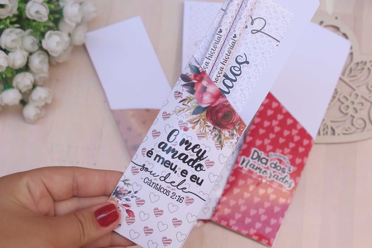 Arquivo Digital Lembrancinha Cristã para Encontro de Casais 3 Mão segura marcador de página impresso com texto romântico e flores.