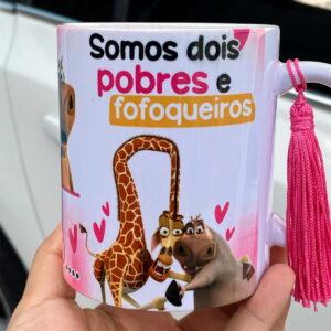 Artes PNG Gloria Madagascar para Canecas Pobre e Fofoqueira 26 Mão segurando caneca branca estampada com desenhos de animais e frase em português.
