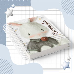 Caderno espiral com ilustração de coelhinho desenhado estilo aquarela sobre fundo quadriculado azul.