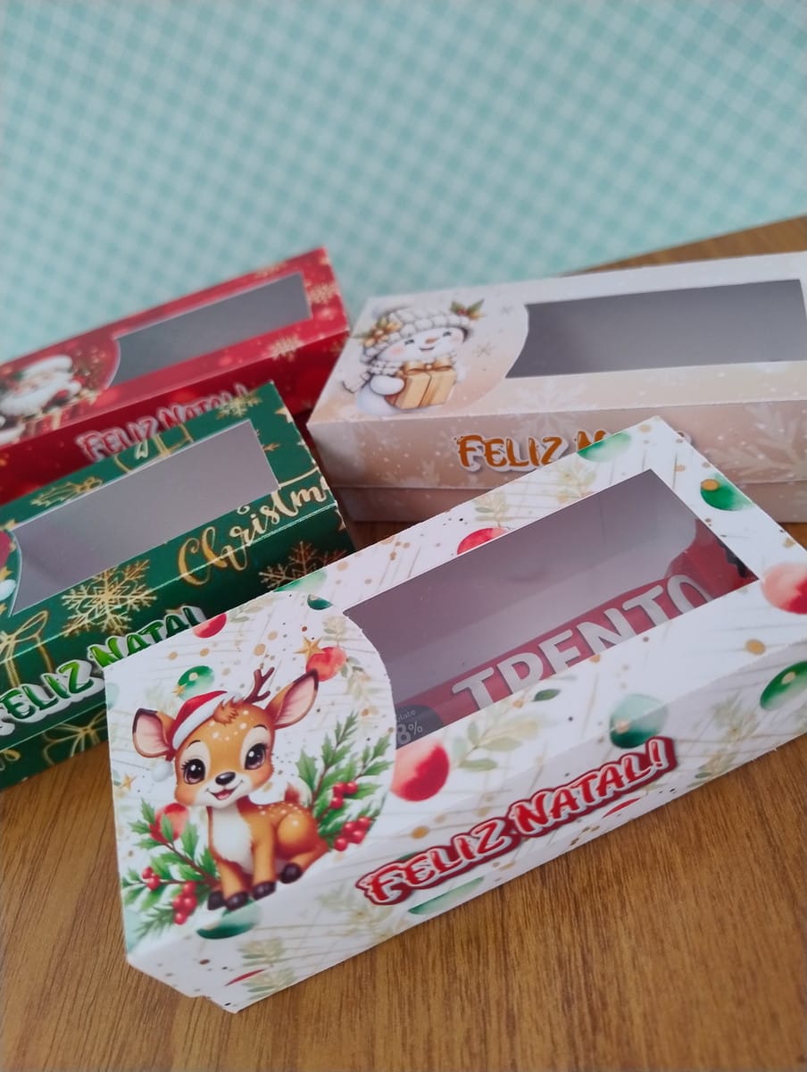 Caixinhas de Natal Vintage em PNG e PDF 3 Caixas de papel decoradas com temas natalinos sobre uma mesa de madeira.