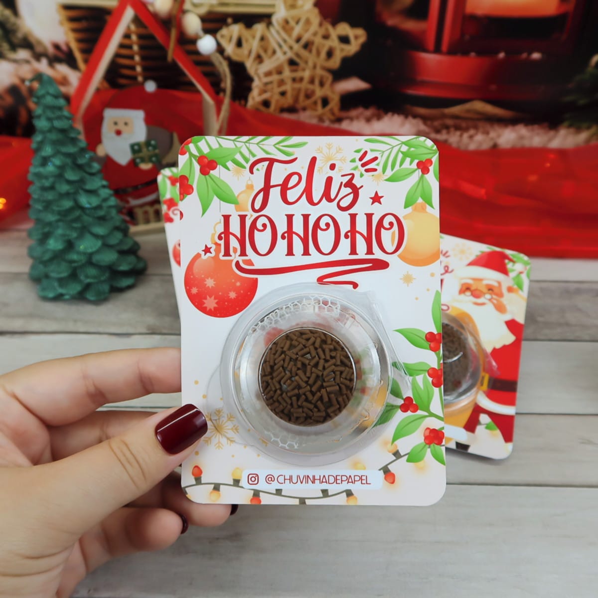 Card Blister Natal 2023 Digital para Embalagens Festivas 3 Mão segurando suporte decorativo natalino com doce de chocolate e confeitos em fundo temático.