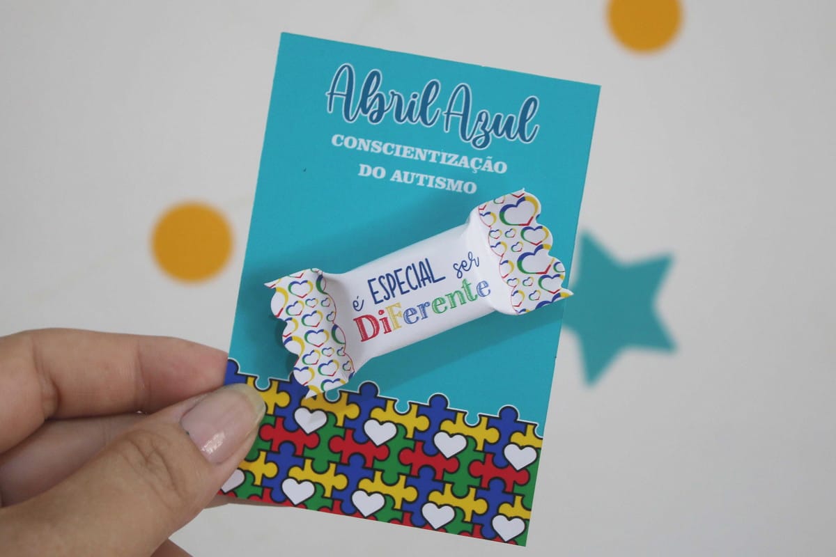 Card e Balas Autismo Arquivo Digital para Imprimir 1 Mão segurando arte digital de cartão azul com tema de autismo.