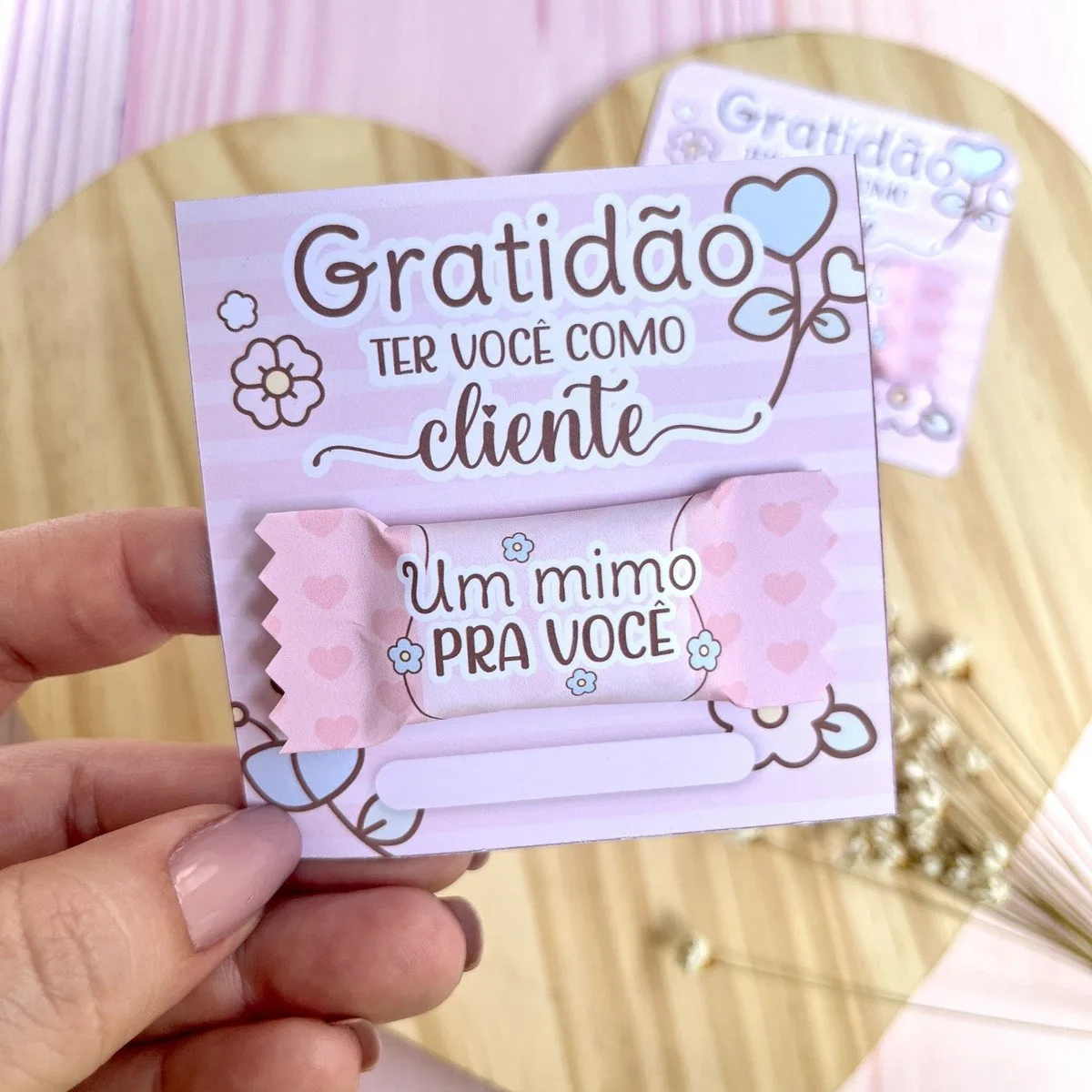 Card e Balinha Mimos Clientes 2 Mão segurando cartão com mensagem de agradecimento e um doce em embalagem rosa.