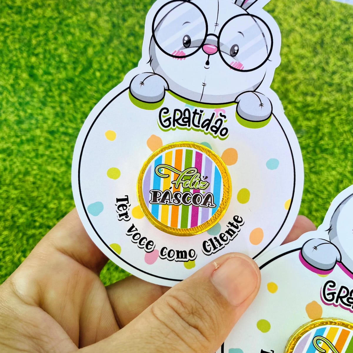 Card Moedinha de Páscoa Digital para Imprimir 5 Mão segurando cartão com desenho de coelho e chocolate de Páscoa ao centro.