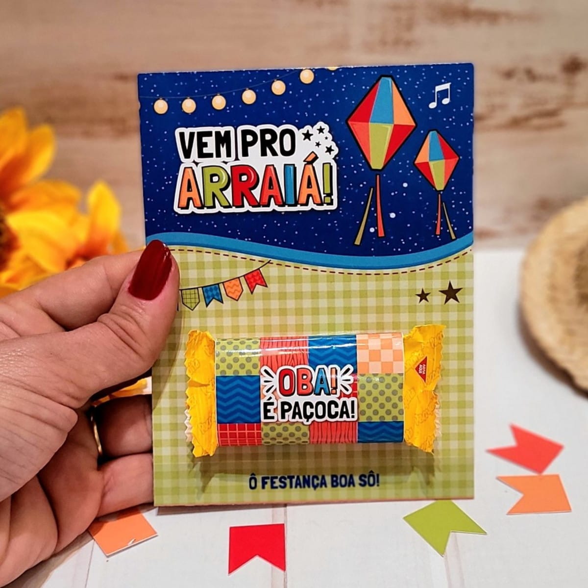 Card Paçoca Festa Junina PNG e PDF para Imprimir 2 Mão segurando cartão decorativo temático com paçoca sobre fundo quadriculado e estrelado.