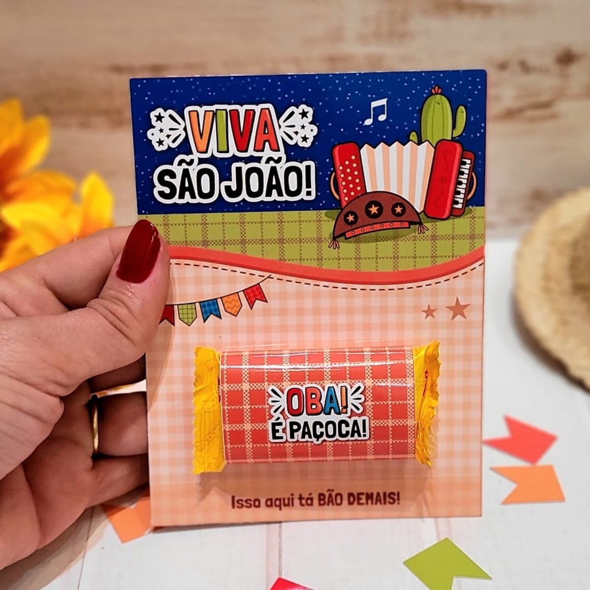 Card Paçoca Festa Junina PNG e PDF para Imprimir 3 Mão segurando cartão decorado com tema de festa junina e doce de amendoim.