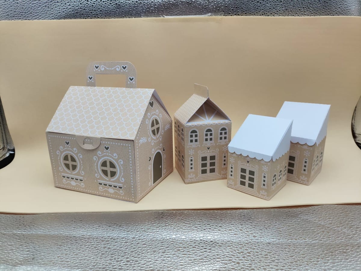 Casinha de Natal Gingerbread em PDF e Studio 4 Quatro caixas de papel em formato de casinhas decoradas com desenhos brancos.
