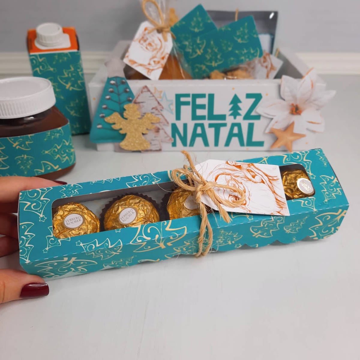 Cesta Natalina Verde em Arquivo de Corte Digital 3 Mão segurando caixa de doces personalizada com embalagem decorativa de tema natalino azul.