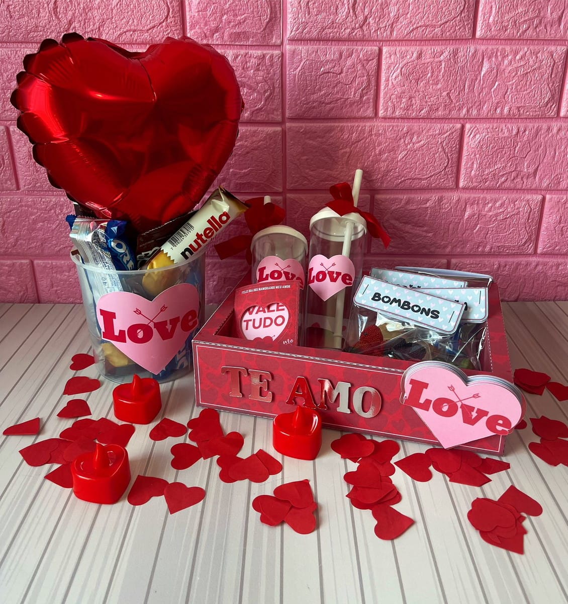 Kit Dia dos Namorados para Imprimir com Artes em Scrapbook 3 Cesta de presentes romântica com balão, doces, copos e corações vermelhos sobre fundo rosa.