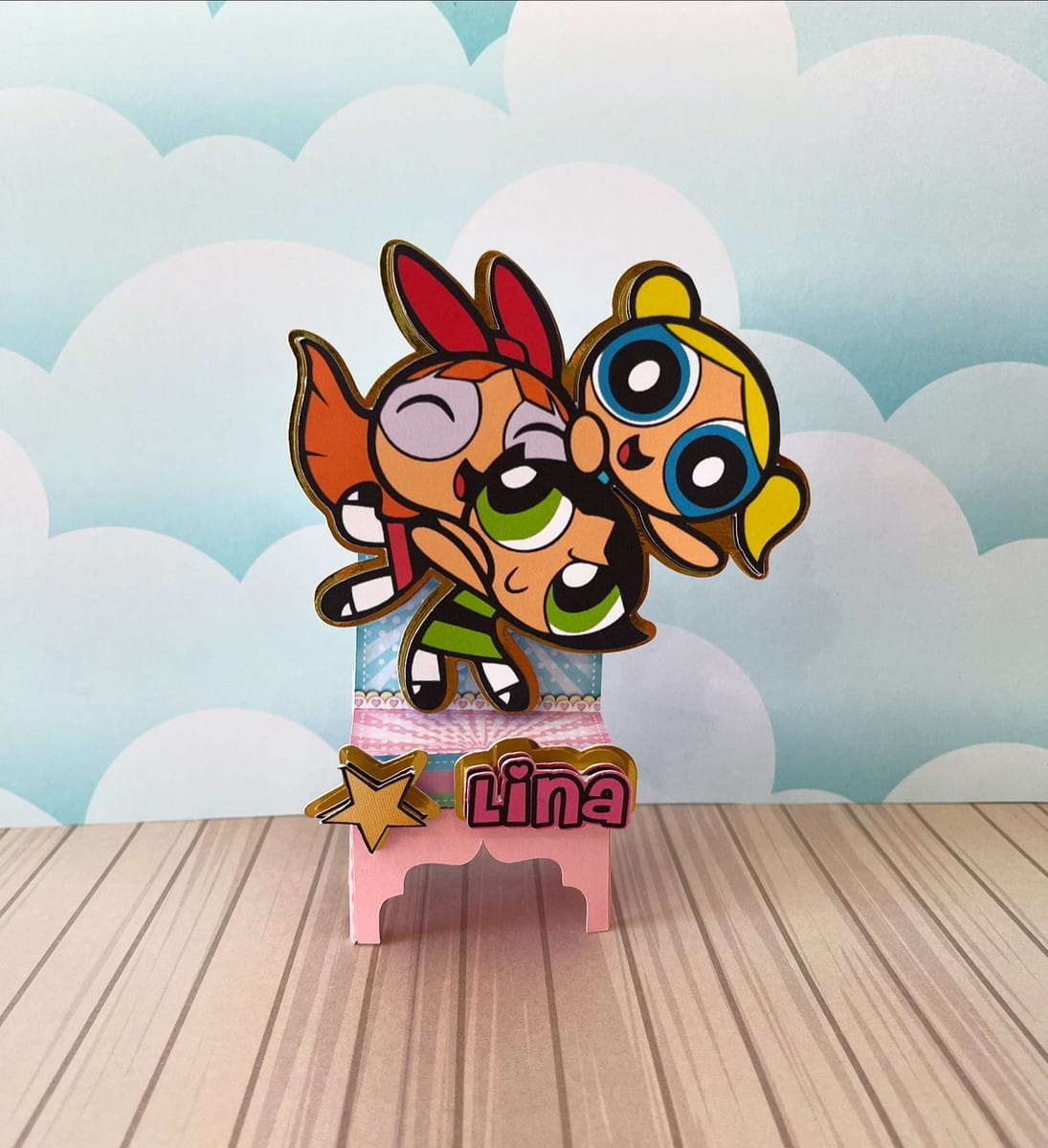Kit Festa Meninas Super Poderosas em PDF e Studio 2 Arte digital de três personagens animadas em pose de voo, com base decorativa.