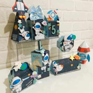 Kit Festa Astronauta Studio Digital para Maquina de Corte 29 Decorações de festa com tema espacial, incluindo caixas e foguetes de papel artesanal.