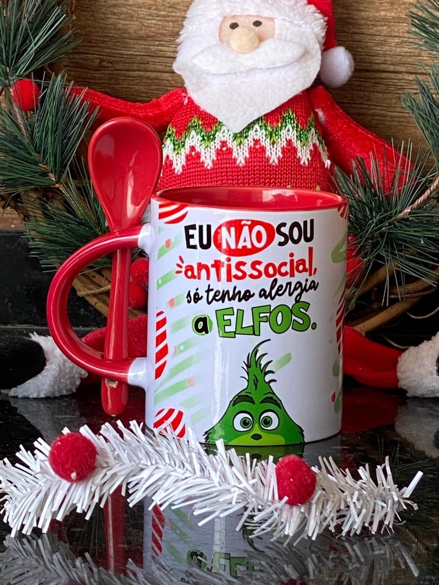 Kit Artes Grinch Debochado para Canecas em PNG e PSD 1 Caneca branca temática de Natal com colher vermelha e enfeites ao fundo