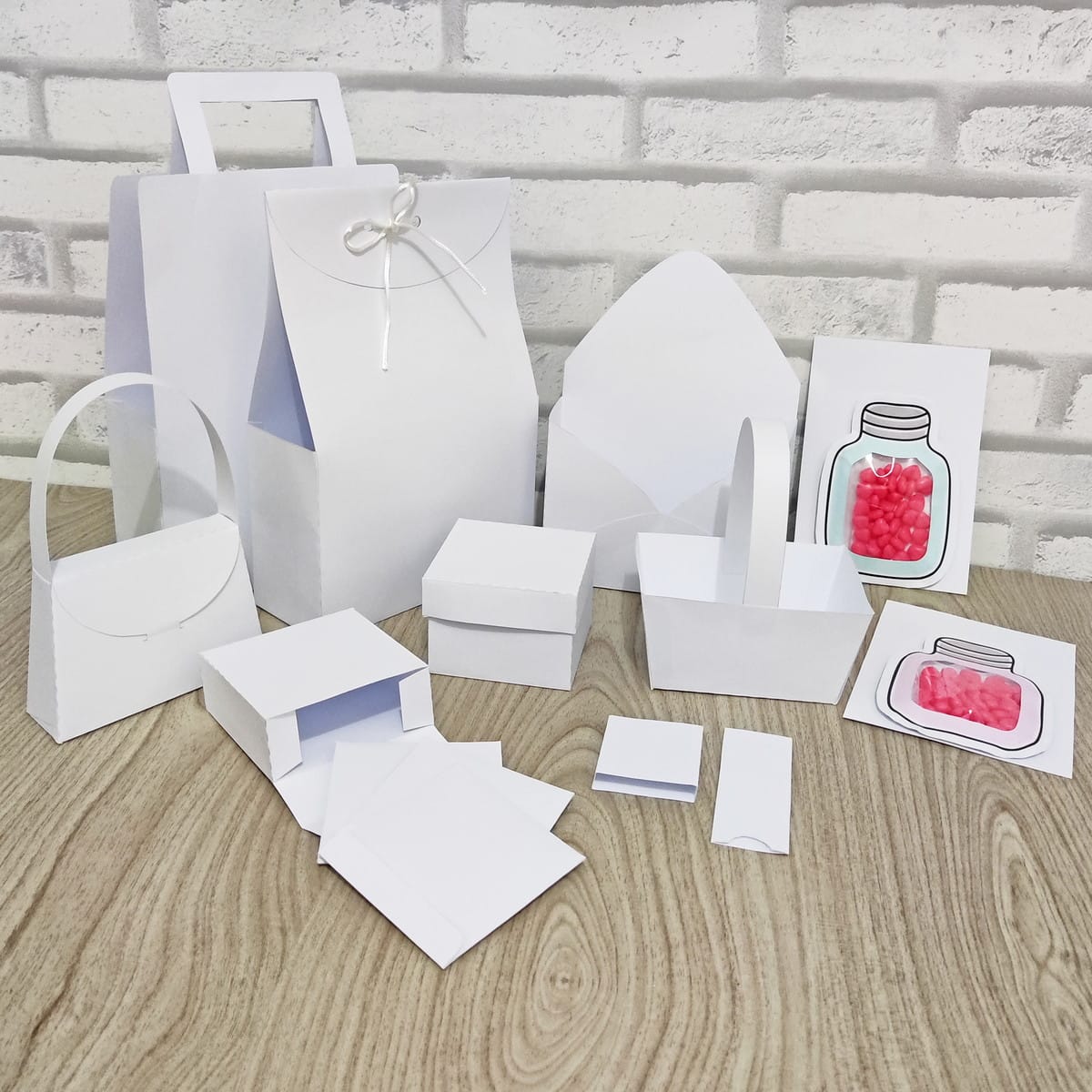 Kit Digital de Moldes Limpos para Papelaria Criativa 2 Diversos itens de papelaria artesanal branca, sacolas, caixas e cartões sobre madeira.