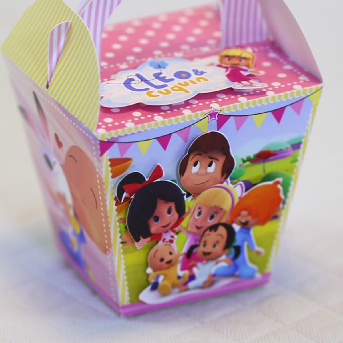 Kit Digital Festa Cleo e Cuquin com Embalagens 2 Caixa de papel decorada com personagens infantis coloridos e alça listrada.