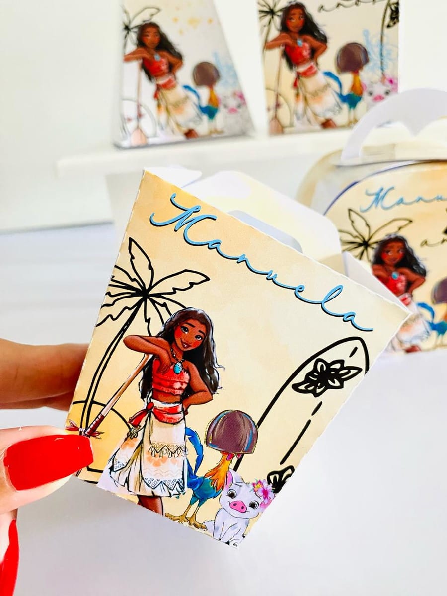 Kit Festa Moana Digital com Arquivo Studio e PDF 3 Mão segurando caixa de lembrancinha personalizada com estampa de personagem animada em fundo bege.