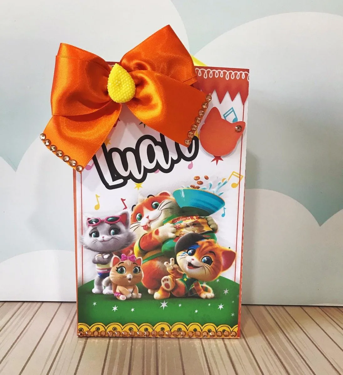 Sacola de papel decorada com gatinhos animados e laço de fita laranja grande.