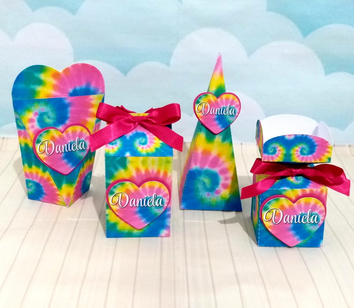 Kit Festa Tie Dye Só um Bolinho com Arquivos Digitais 1 Quatro caixas decorativas de papel com estampa colorida estilo tie dye e laços vermelhos.