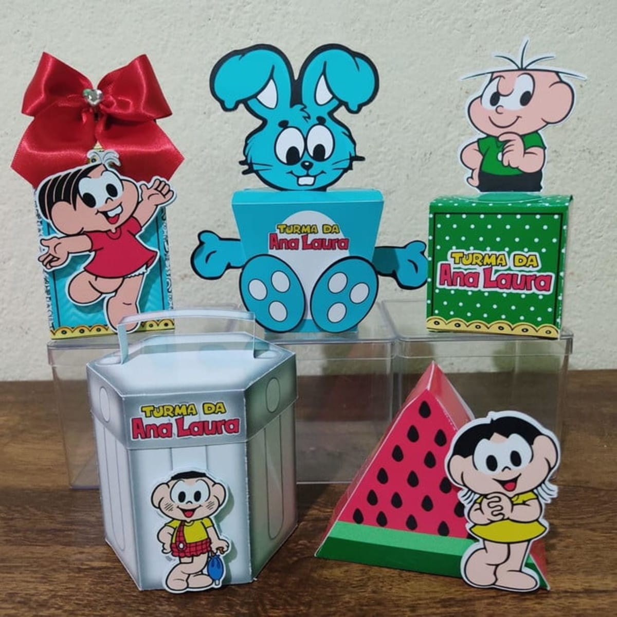 Kit Festa Turma da Monica Studio Artes Vetoriais para Corte 1 Conjunto de caixas decoradas com personagens de desenho animado sobre uma mesa.