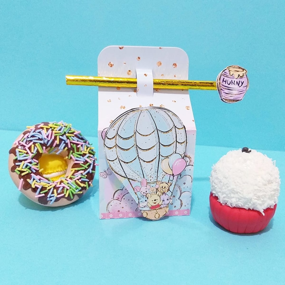 Kit Festa Ursinho Pooh Digital com Caixas para Imprimir 2 Arte digital de caixa decorada com balão, donut e doce em fundo azul.