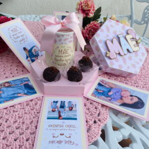 Caixa de presente rosa aberta com fotos, doces e um cofrinho decorado.