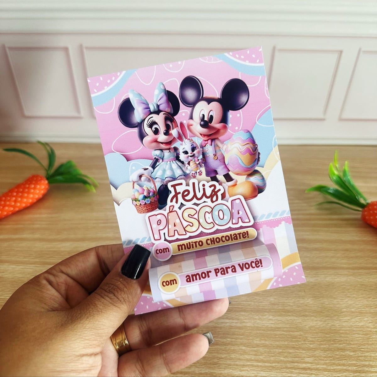 Kit Mimos de Páscoa Minnie e Mickey Digital 2 Mão segurando cartão decorado com personagens de desenho animado e tema de Páscoa.