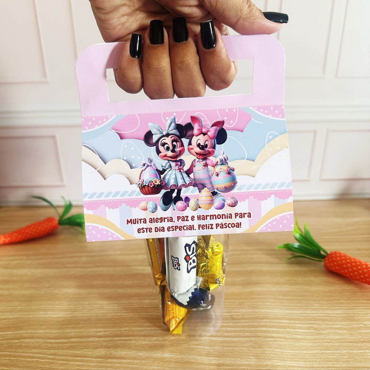 Kit Mimos de Páscoa Minnie e Mickey Digital 4 Mão segurando embalagem temática com personagens infantis, ovos de páscoa e chocolates dentro.