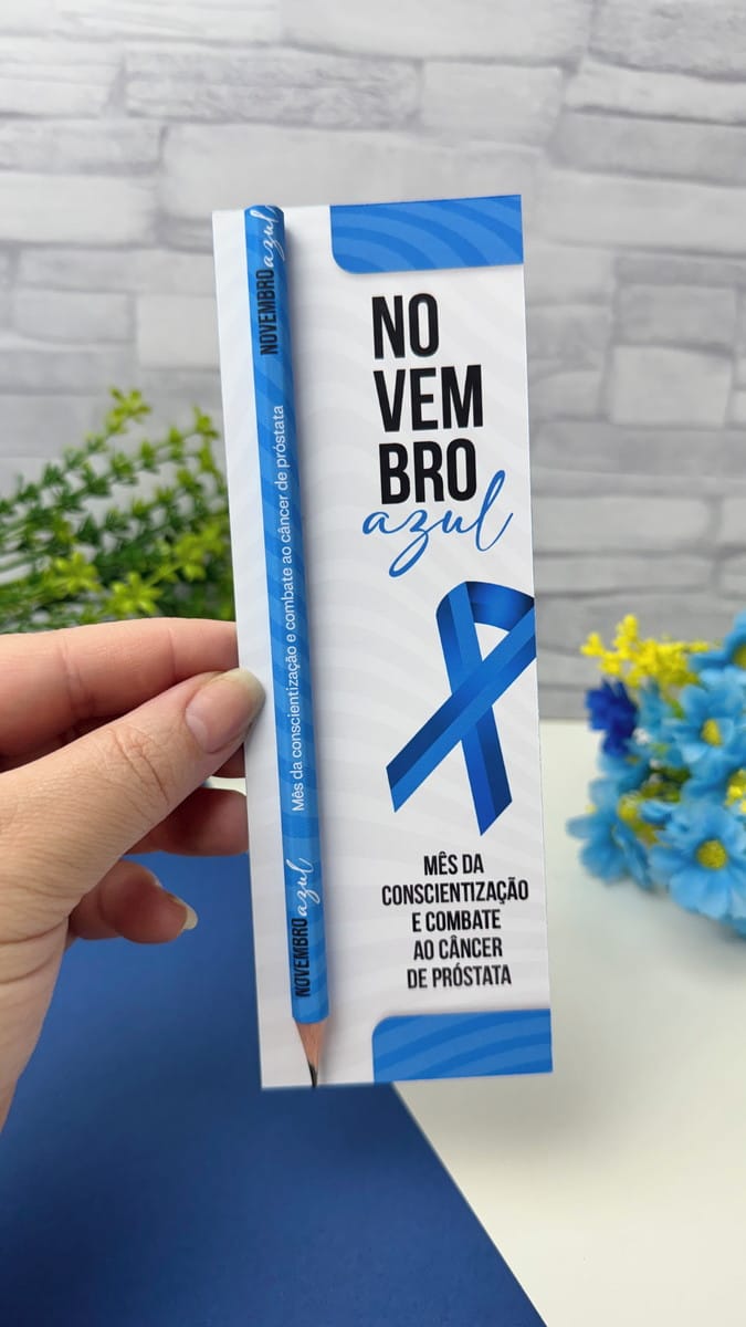 Kit Mimos Novembro Azul 2025 Arte Digital em Alta Resolução 2 Mão segurando suporte de papel branco com lápis azul personalizado com laço
