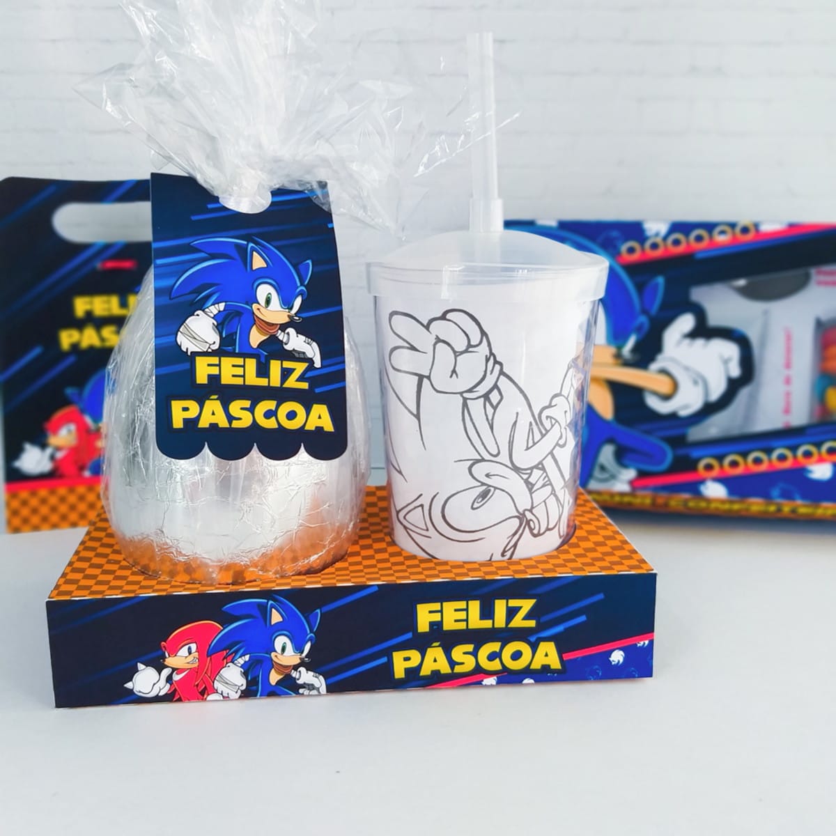 Arquivo Digital Kit Páscoa Sonic para Confeiteiros 3 Ovo de Páscoa embrulhado em prata, copo transparente com ilustração de personagem, e embalagens temáticas.