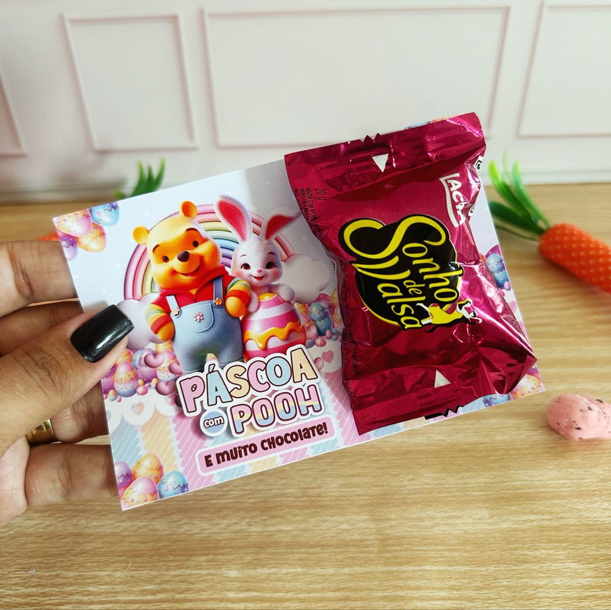 Kit Páscoa Ursinho Pooh Digital com Artes para Embalagens 3 Mão segurando cartão decorado com tema de páscoa e um bombom de chocolate