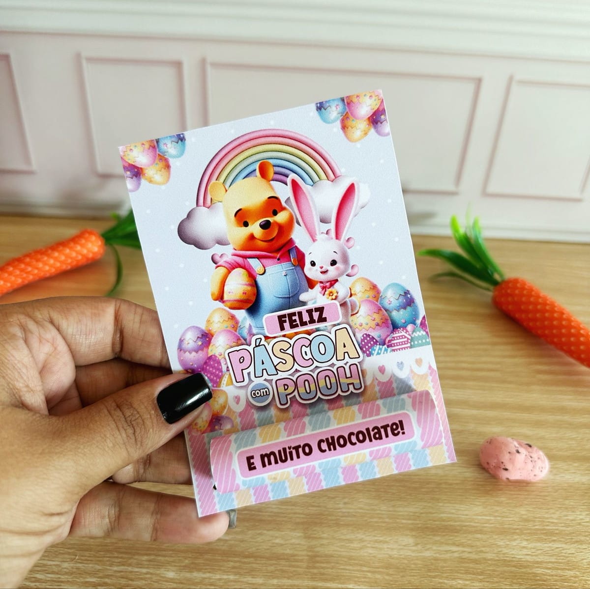 Kit Páscoa Ursinho Pooh Digital com Artes para Embalagens 4 Mão segurando cartão decorativo de páscoa com urso e coelho ilustrados.