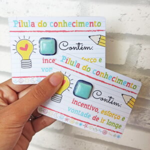 Mão segura cartões decorados com desenhos coloridos e pequenos objetos brilhantes colados.