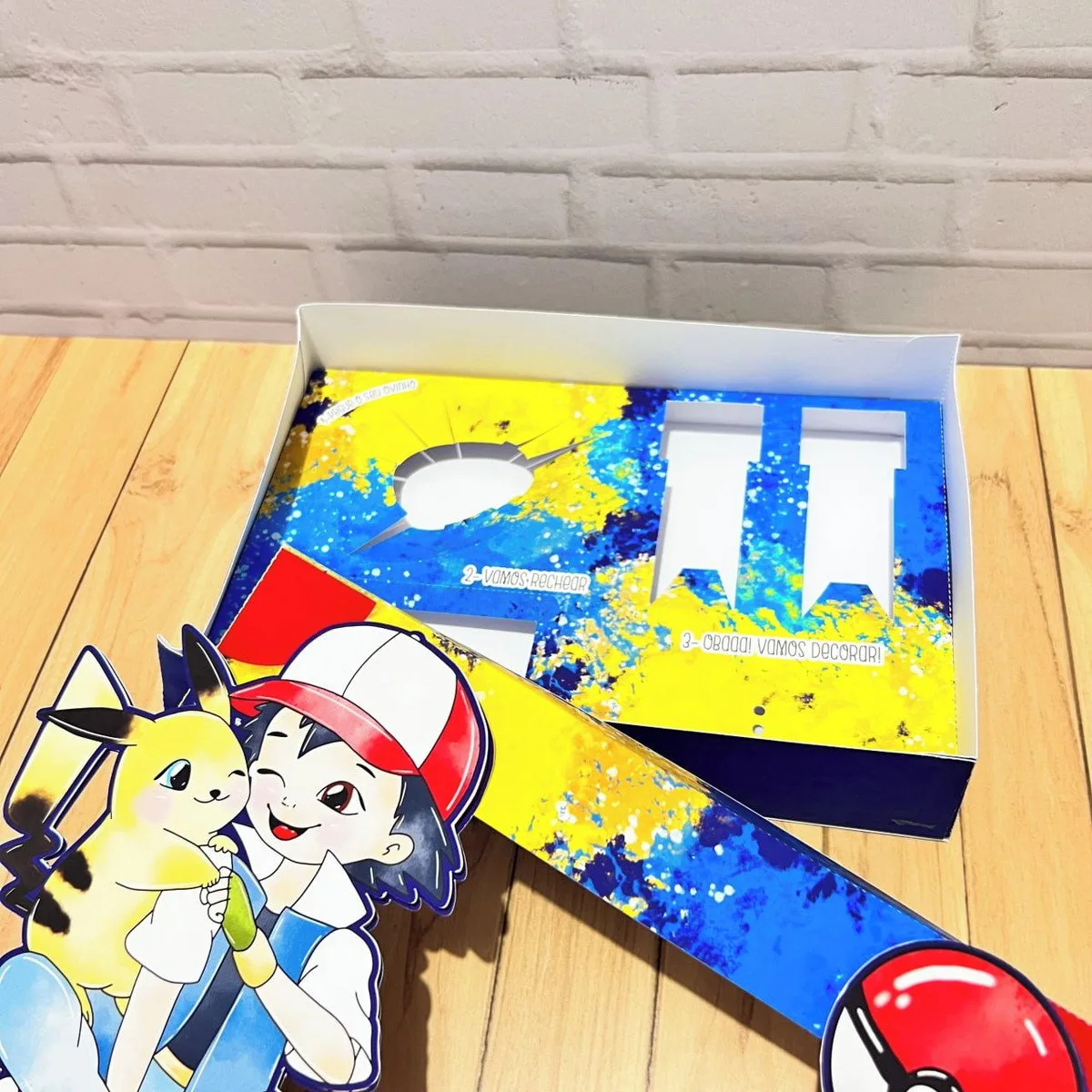 Mini Confeiteiro Páscoa Pokémon 2 Caixa de papelão aberta e personalizada com ilustrações coloridas sobre fundo de madeira.