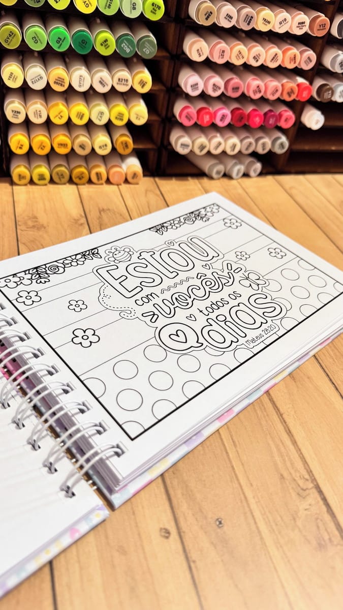 Pack Livro de Colorir Versículos Bíblicos para Sublimação 5 Caderno de colorir espiral aberto com frase escrita em português sobre fundo de madeira.