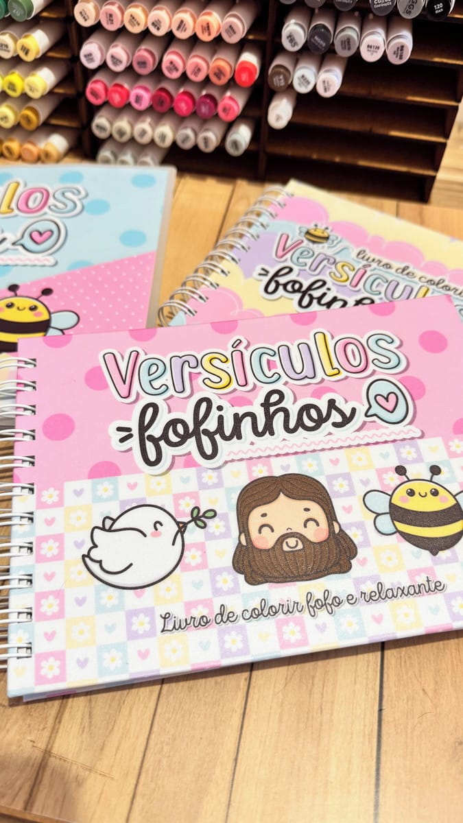 Pack Livro de Colorir Versículos Bíblicos para Sublimação 1 Cadernos coloridos e ilustrados sobre uma mesa de madeira com organizador de canetas ao fundo