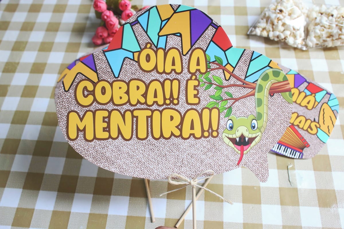 Plaquinhas de Festa Junina Arquivo de Corte para Imprimir 3 Placa decorativa temática com desenho de cobra e frase em fundo de estopa bege.