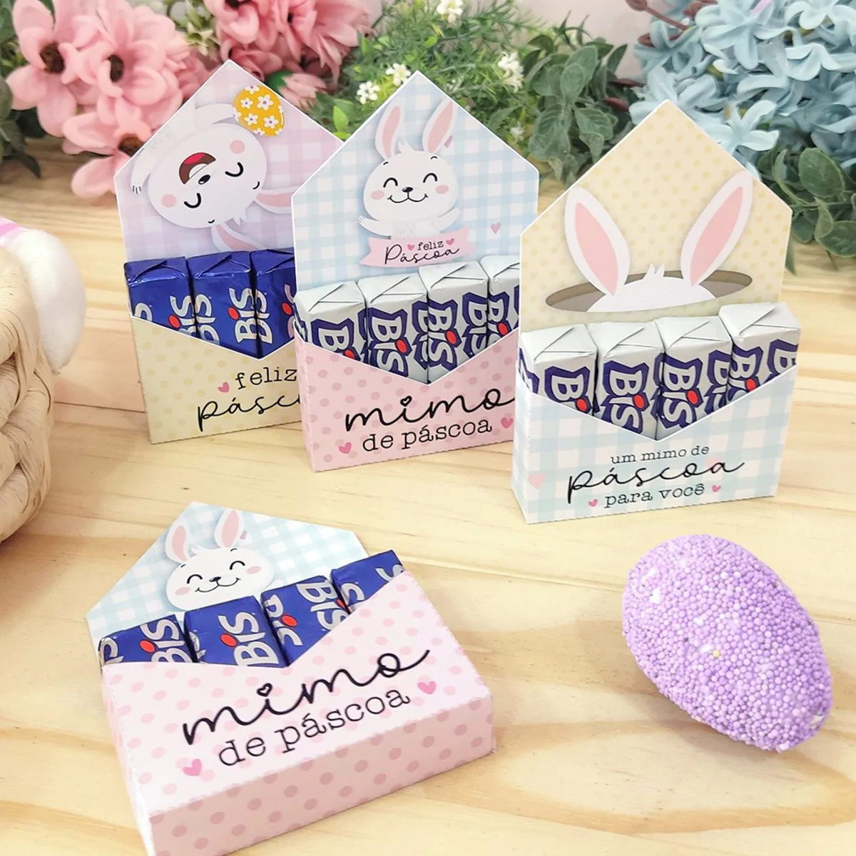 Porta Bis Páscoa 4 Caixinhas de papel decoradas com tema de coelho e chocolate recheadas em fundo de madeira.