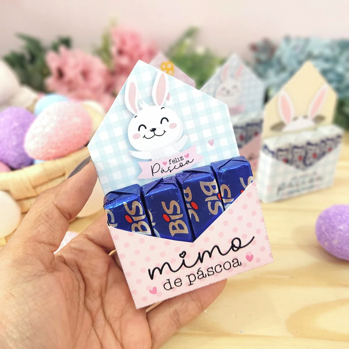 Porta Bis Páscoa 1 Mão segura uma pequena caixa temática de Páscoa contendo chocolates azuis.