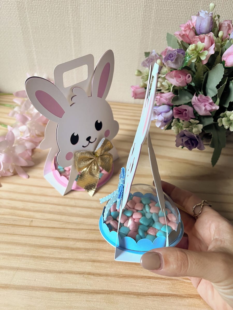 Sacolinha Coelhinha com Alça Arquivo Digital para Festas 4 Caixas de papel em forma de coelho contendo doces coloridos em cúpulas transparentes.