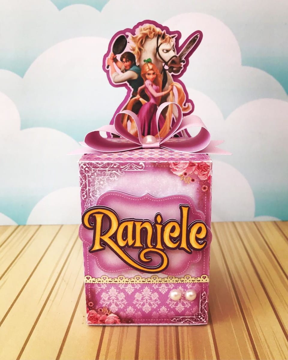 Arquivo Festa Rapunzel com Caixas Convite e Topo de Bolo 4 Design de caixa decorativa rosa com personagens animados e laço festivo.